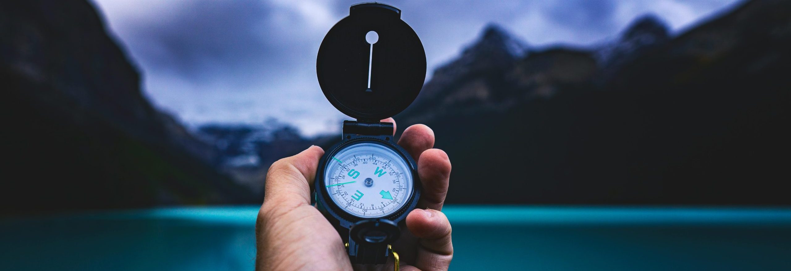 A hand holding a compass with a serene lake and mountains in the background, capturing the spirit of adventure.