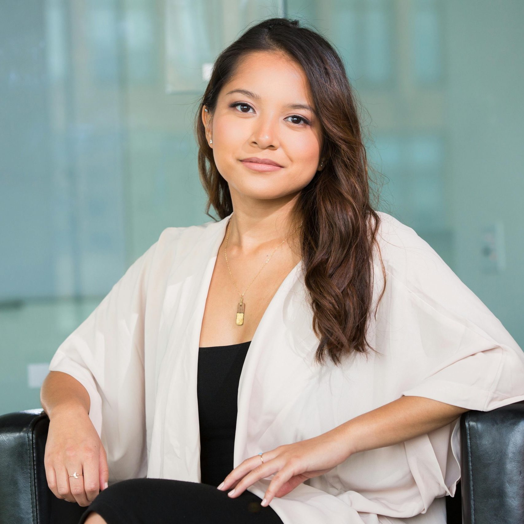 A professional Asian businesswoman sitting confidently in a modern office setting.