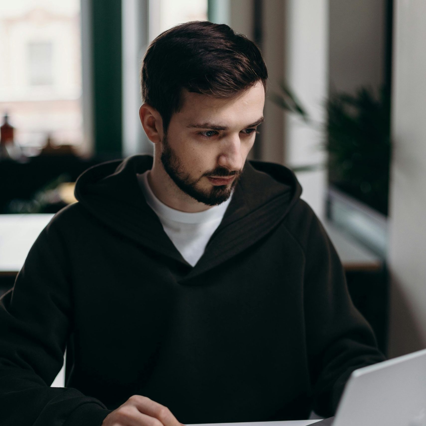 A focused young man using a laptop at a desk in a stylish home office setting.