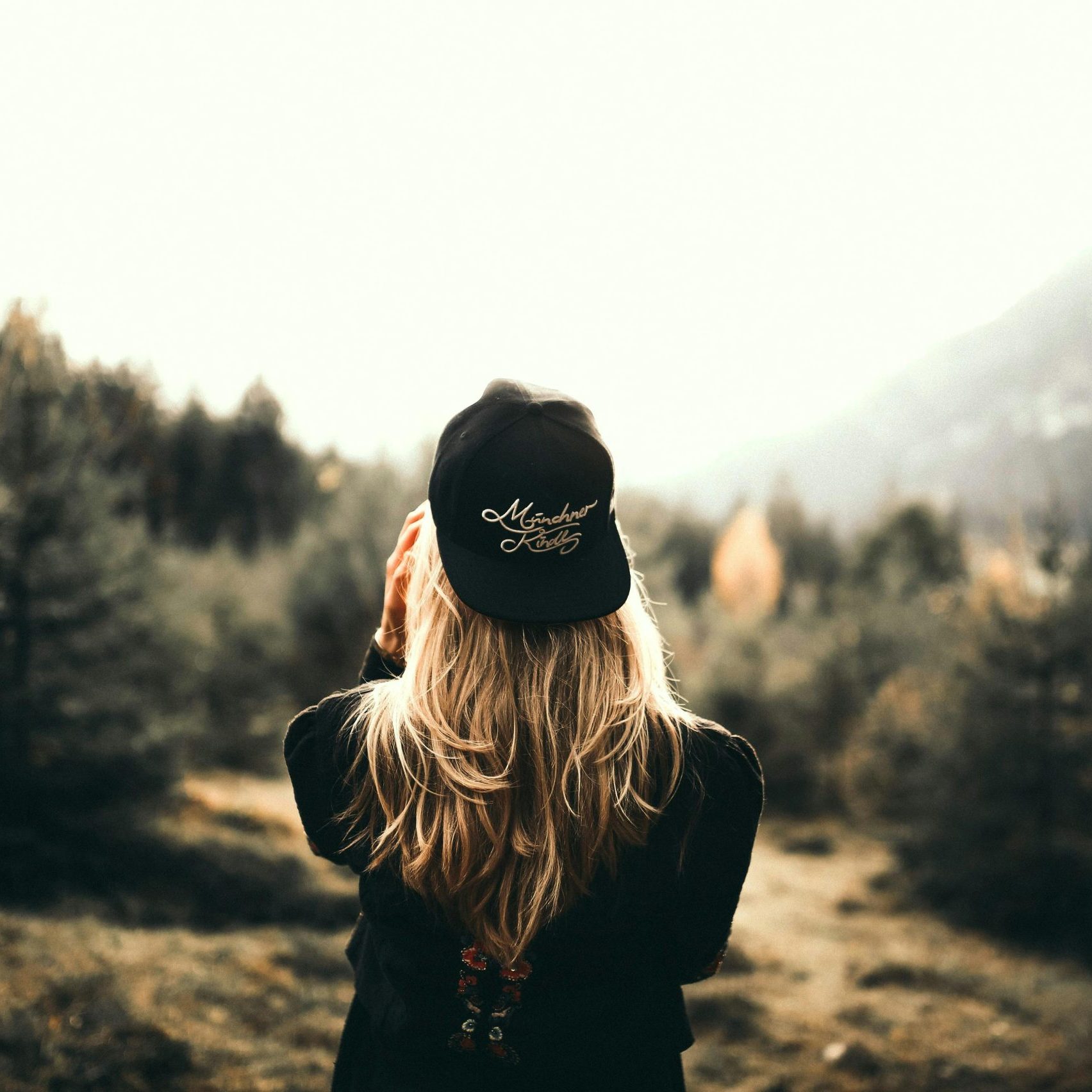 A woman in black cap and sweater enjoys a mountain view, embracing outdoor adventure.